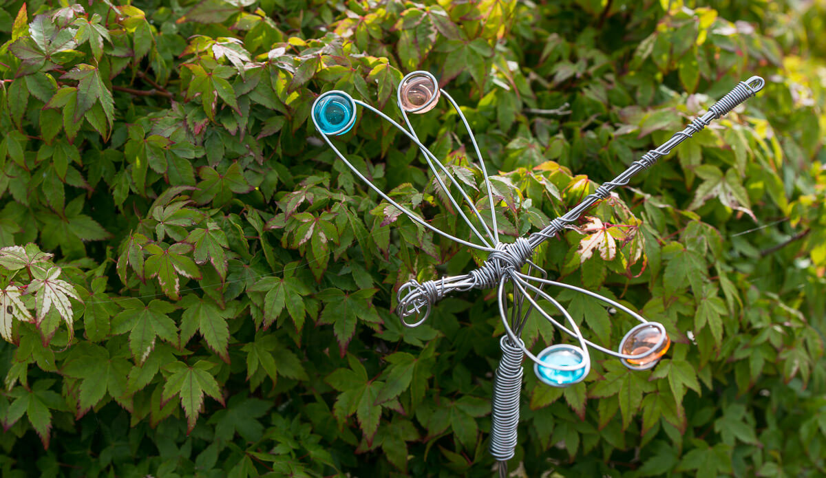 Decorative metal dragonfly with colorful glass beads on a green leafy background