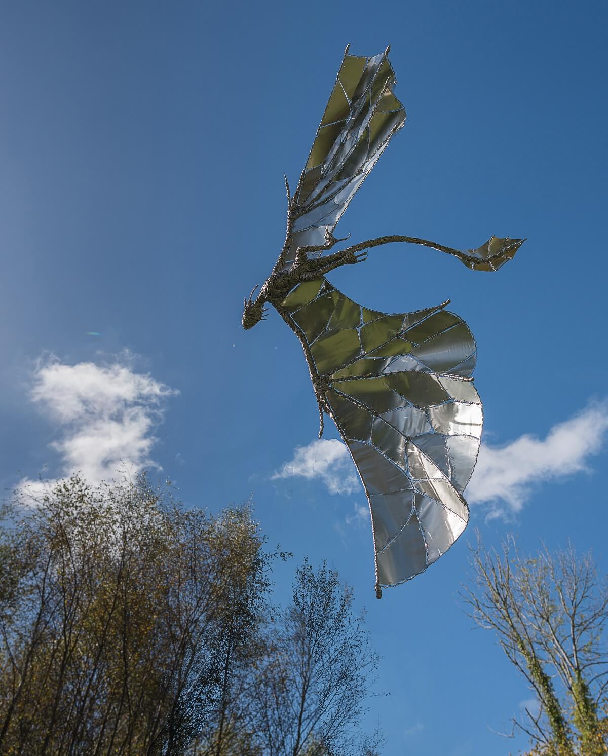 Stainless steel and recycled metal dragon flying against blue sky