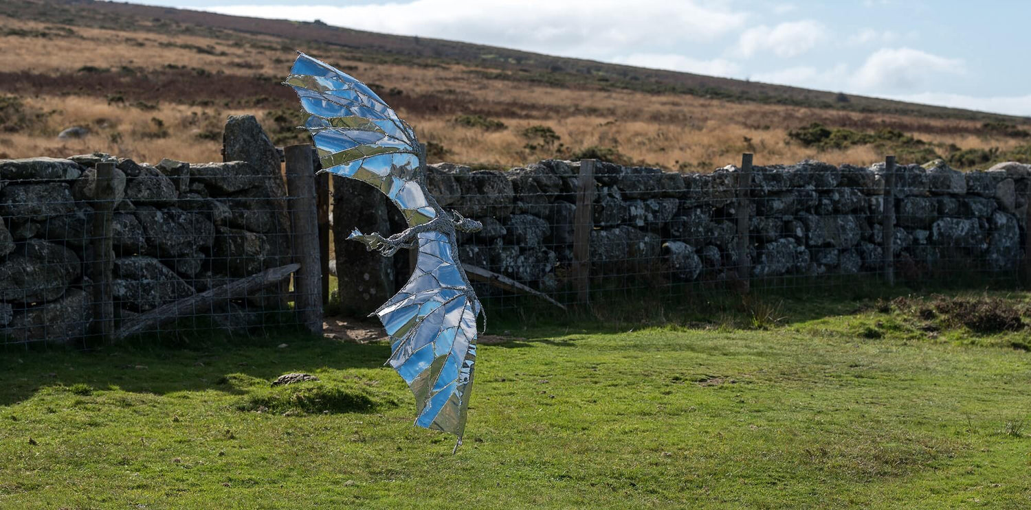 Stainless steel dragon flying sculpture near rock wall Dartmoor