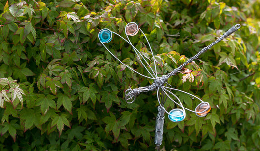 Decorative metal dragonfly with colorful glass beads on a green leafy background
