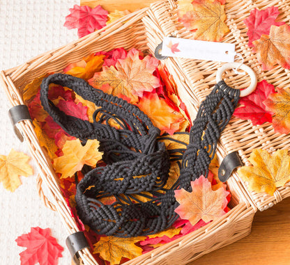 Black macrame plant hanger in a wicker basket surrounded by colorful autumn leaves.