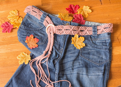 Macrame belt in blush pink styled with denim jeans and autumn leaves for a fun, versatile look.