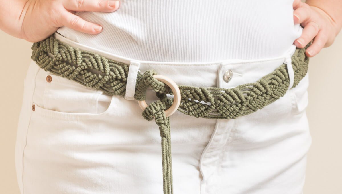 Woman wearing an olive green macrame belt tied around white jeans adding a fun, stylish touch.