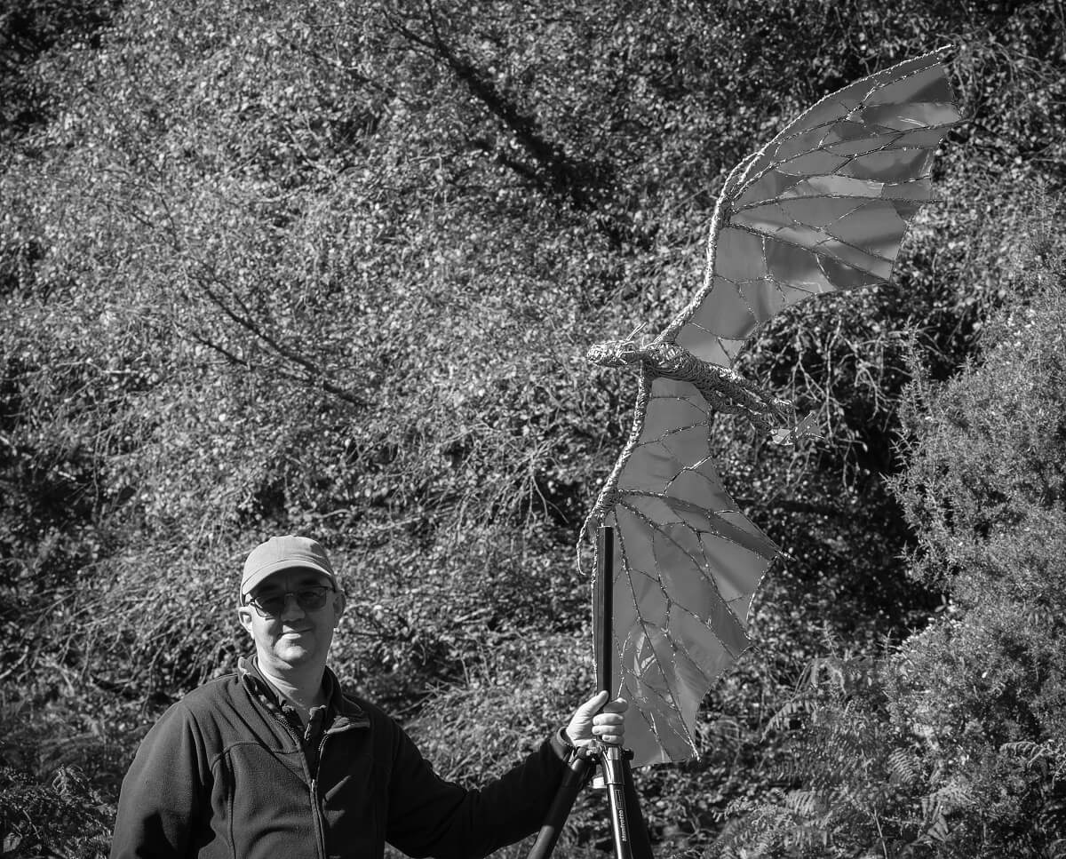 Stainless steel dragon sculpture on tripod being held by assistant black and white image